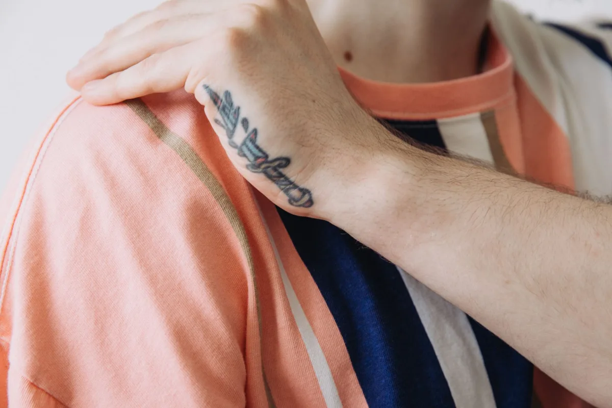 A detailed close-up of a hand with a dagger tattoo resting on a striped shirt.
