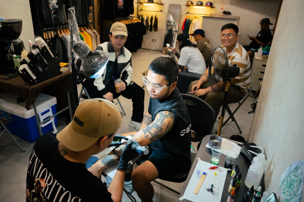 Tattoo artist creating a detailed design in a vibrant and busy studio setting.