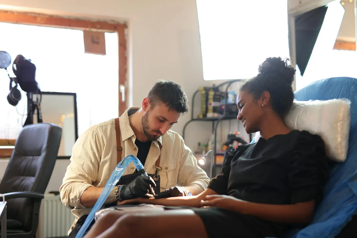 A tattoo artist carefully creating a design in a well-lit studio with a client.