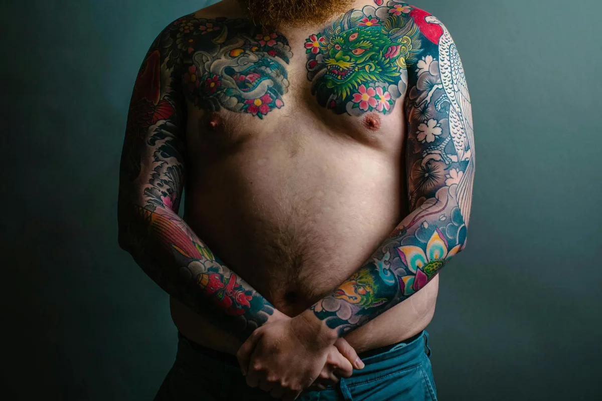 Portrait of a shirtless man with vibrant tattoos on chest and arms.