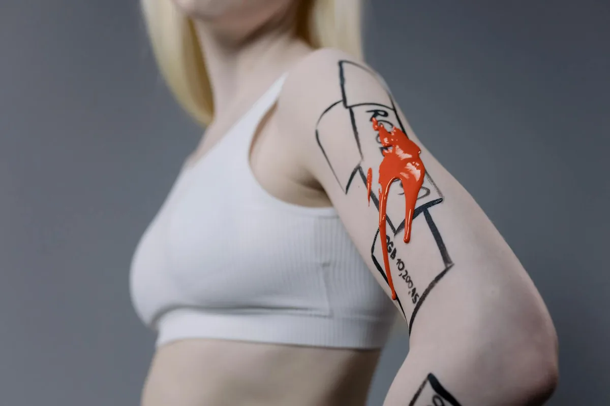 Close-up shot of arm with unique artwork and dripping red paint, captured in a studio.