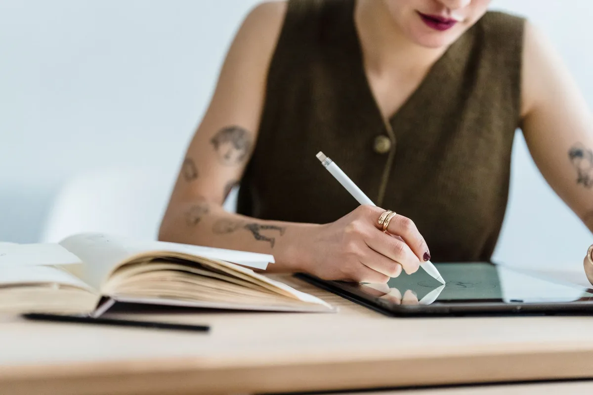 Crop anonymous female designer in casual clothes drawing sketches while siting at wooden table with graphics tablet