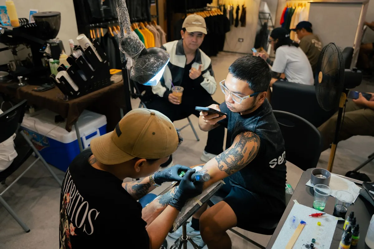 Tattoo artist giving a tattoo to a client in a bustling studio environment.