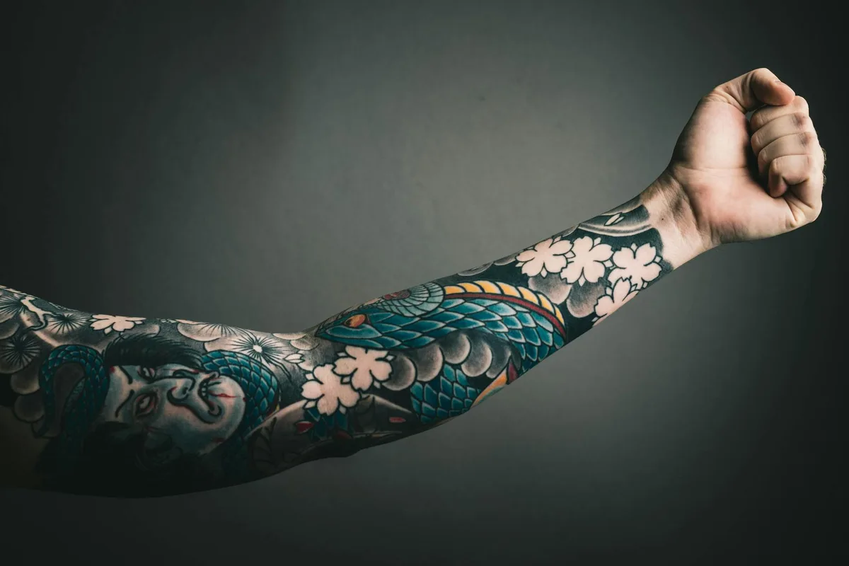 A close-up of a tattooed arm with a colorful sleeve design, featuring floral and artistic elements.