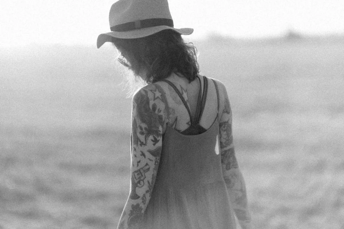 a woman with tattoos and a hat walking in a field