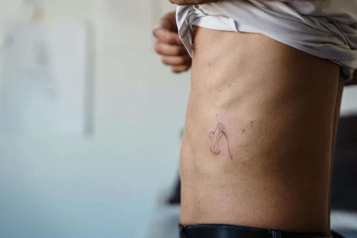 Close-up view of a minimalist tattoo on a person's side torso in an indoor setting.