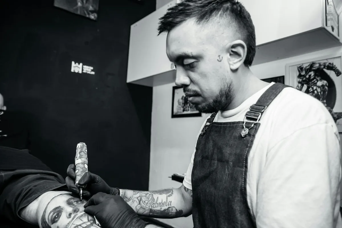Tattoo artist focused on crafting a detailed black ink tattoo on a client's arm indoors.
