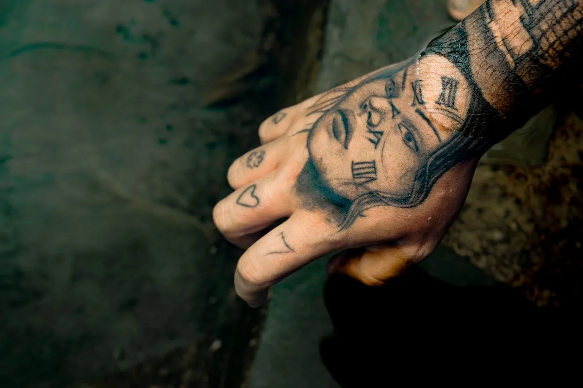 A detailed shot of a hand with expressive tattoos including Roman numerals and faces.
