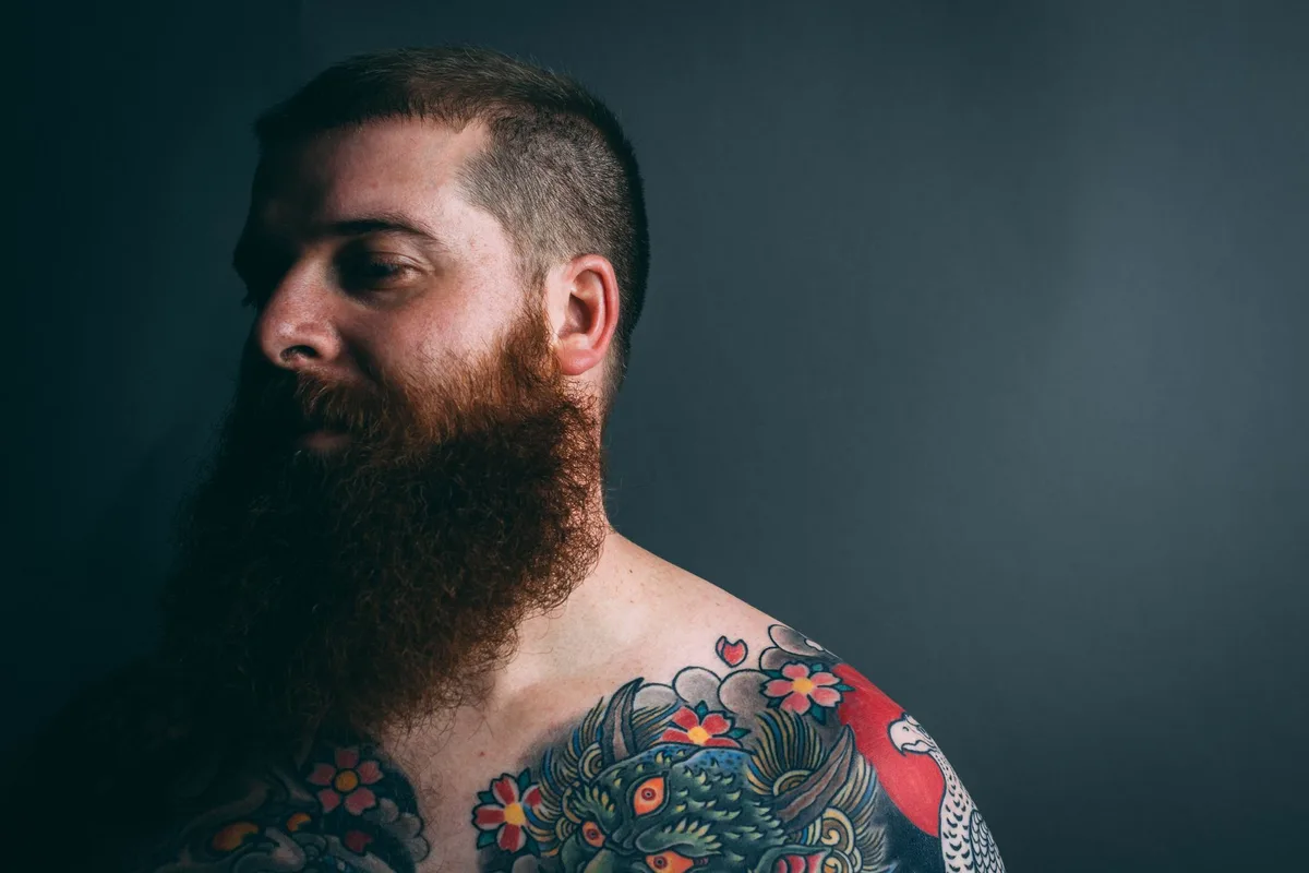Portrait of a tattooed man with a beard in dramatic lighting.