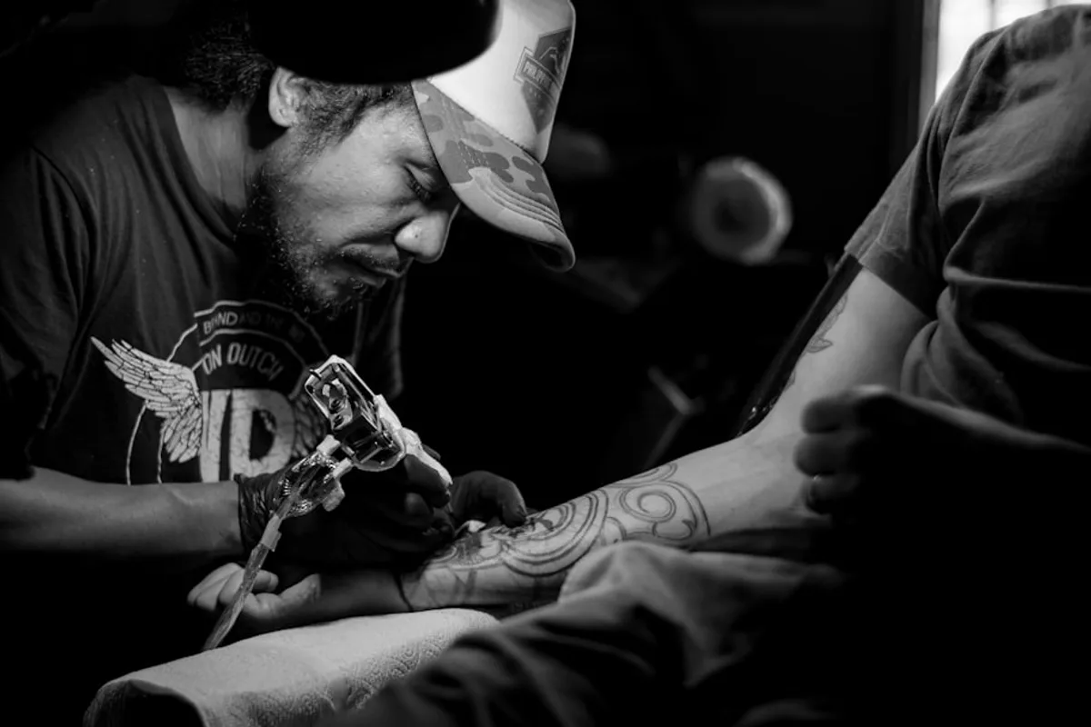 grayscale photo of man doing tattoo