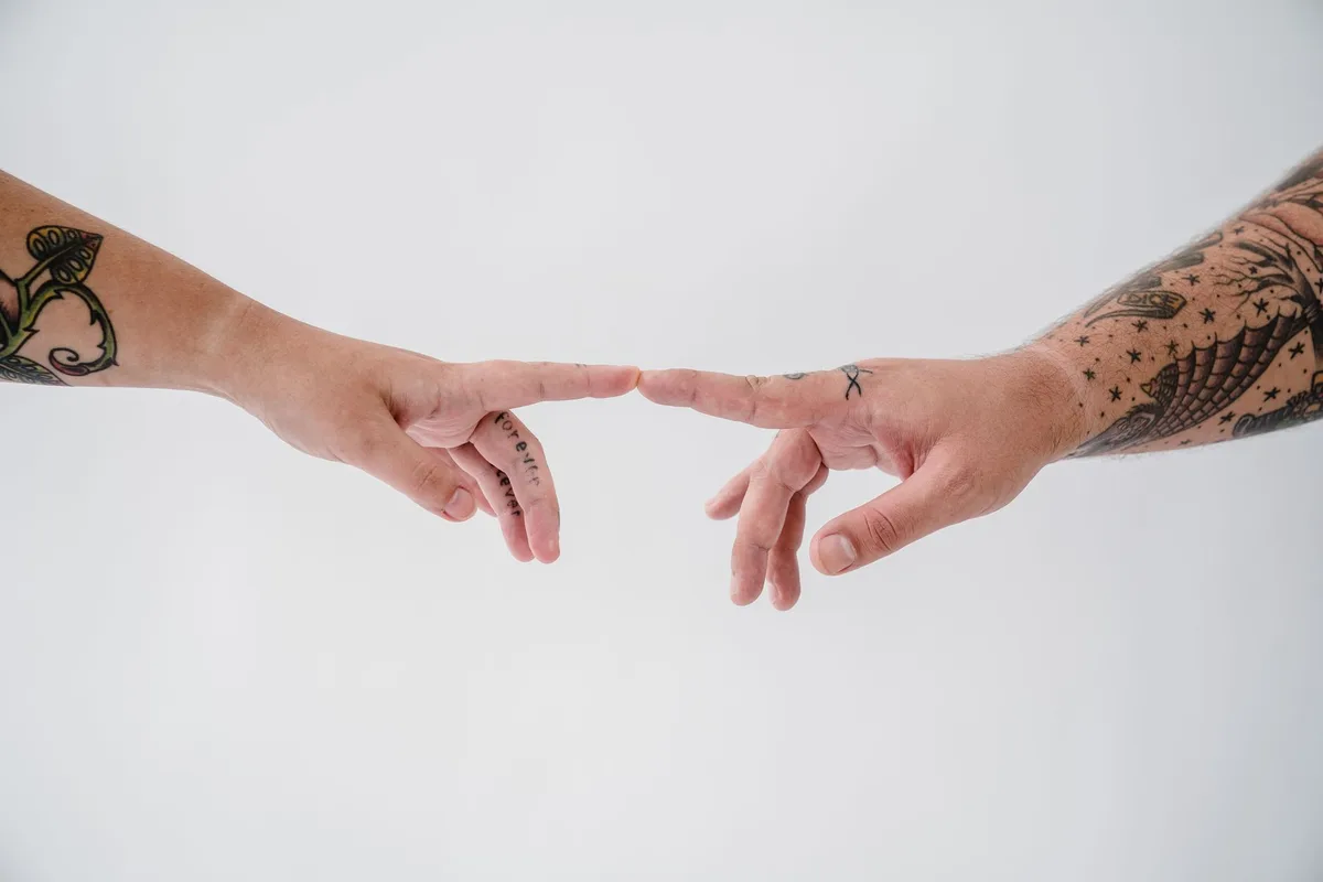 Two tattooed hands reaching out to each other in a minimalist studio setting, capturing a moment of connection.