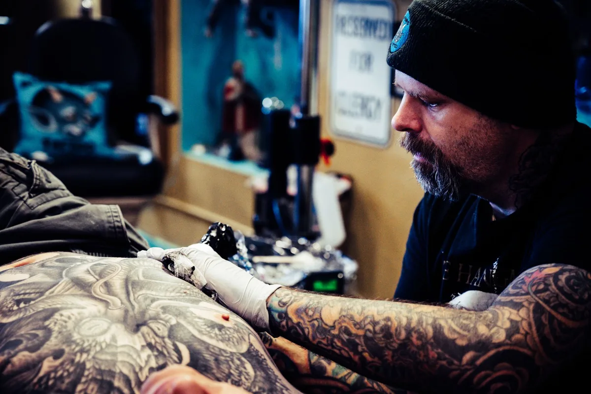 Tattoo artist skillfully inks intricate design on client's back in a tattoo studio.