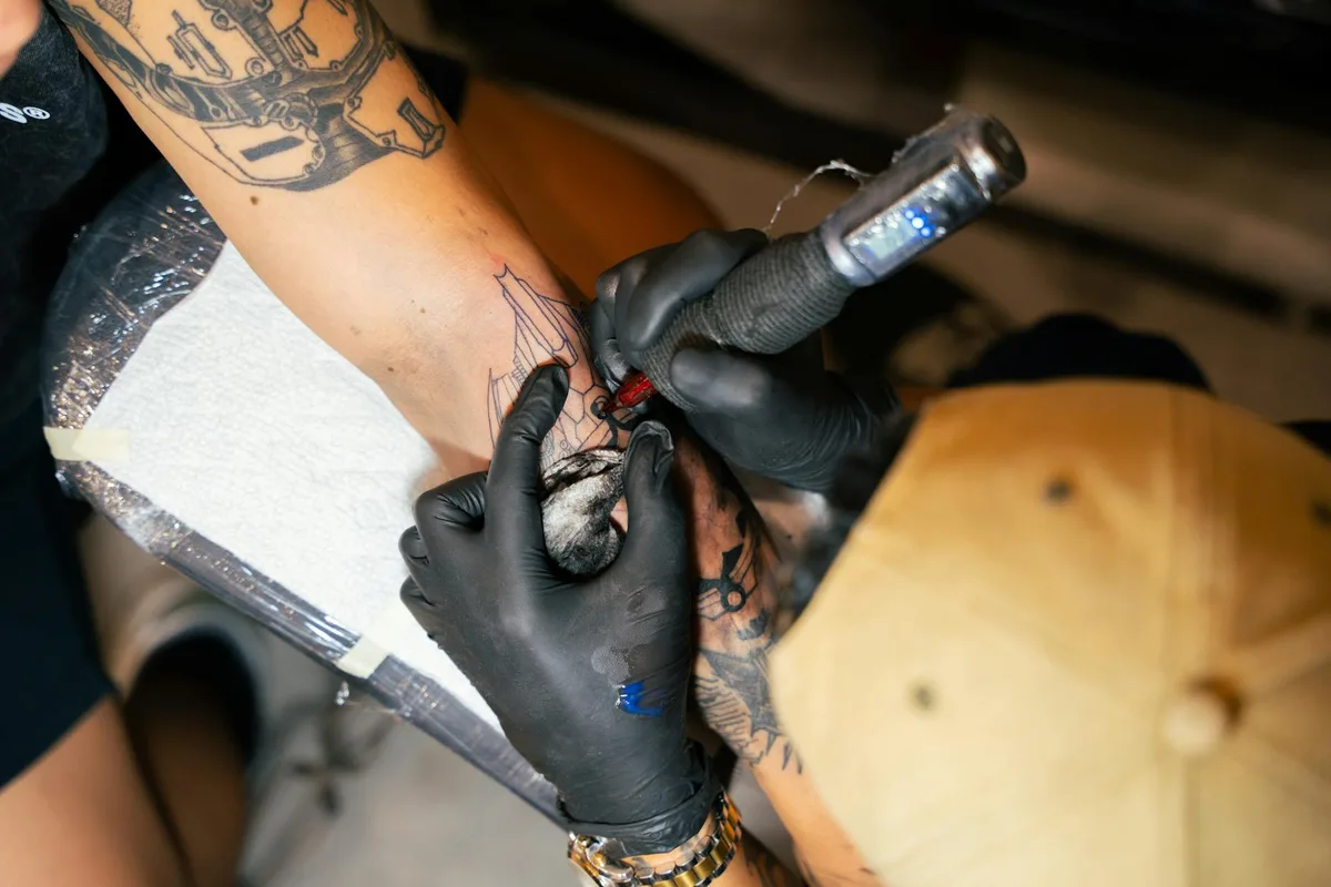 Tattoo artist crafting intricate design on client's arm with precision and care.