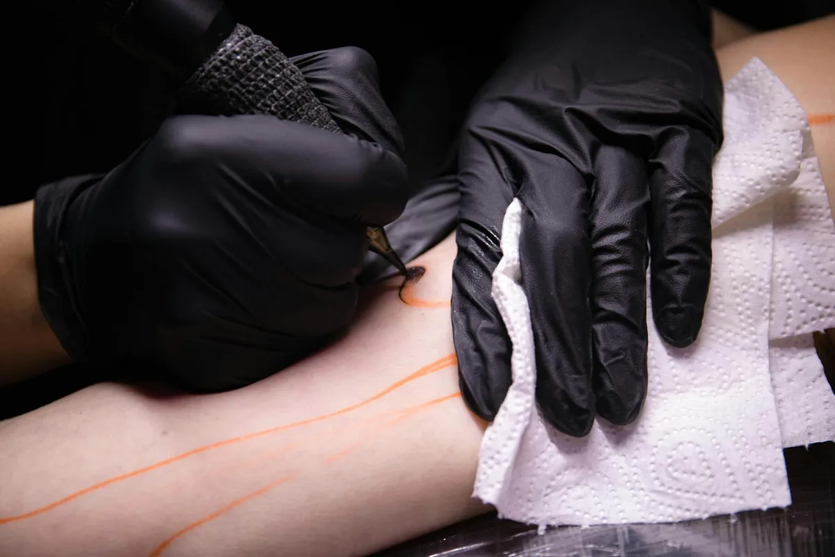 Professional tattoo artist wearing black gloves tattooing an arm with precision.