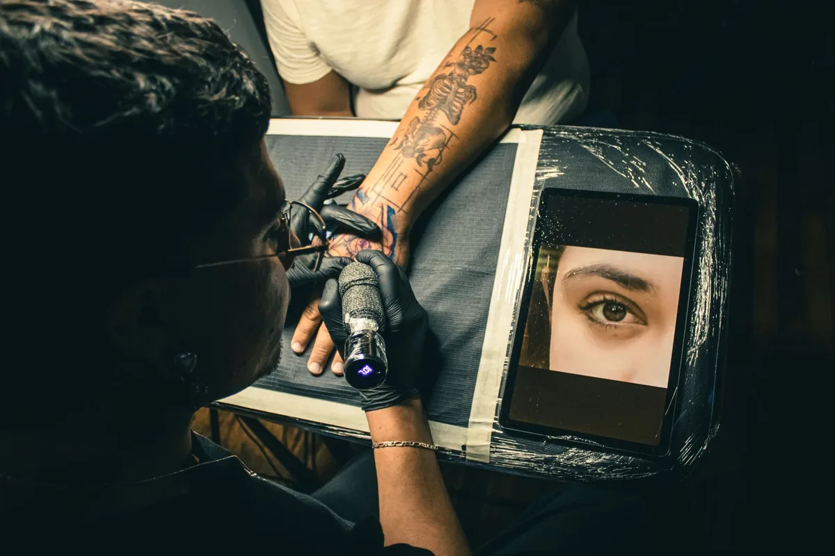 Tattoo artist working on a detailed arm tattoo in a studio setting, showcasing precise craftsmanship.
