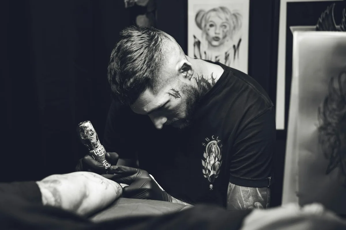 Black and white photo of a focused tattoo artist working in a studio, capturing the art of inking.