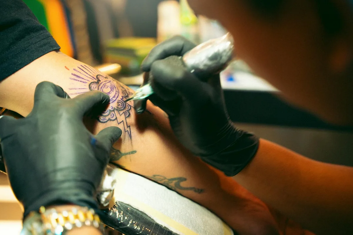 Artist meticulously applying a tattoo on a person's arm in a studio.
