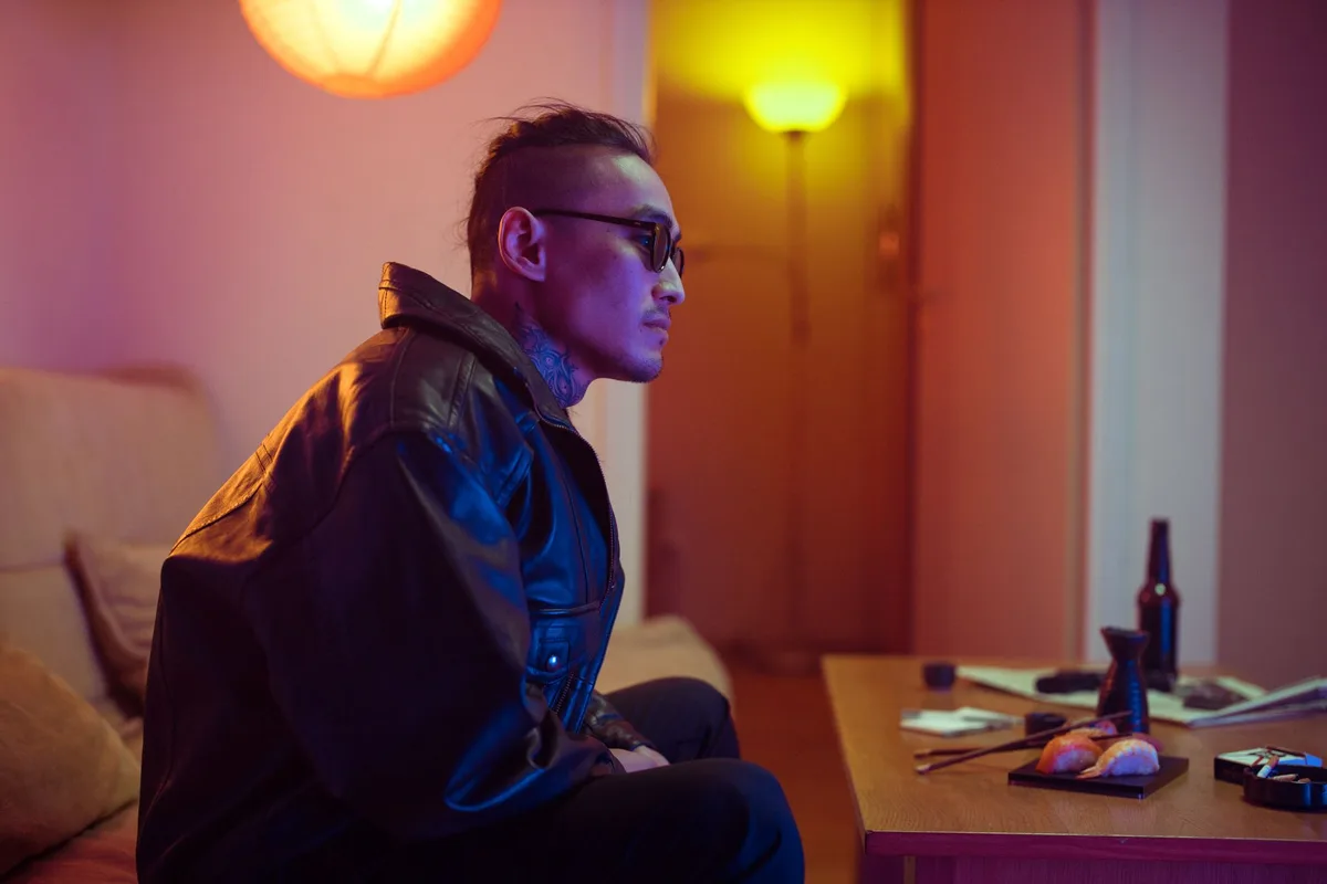 Side view of a man in a leather jacket, sitting indoors with sushi on the table.