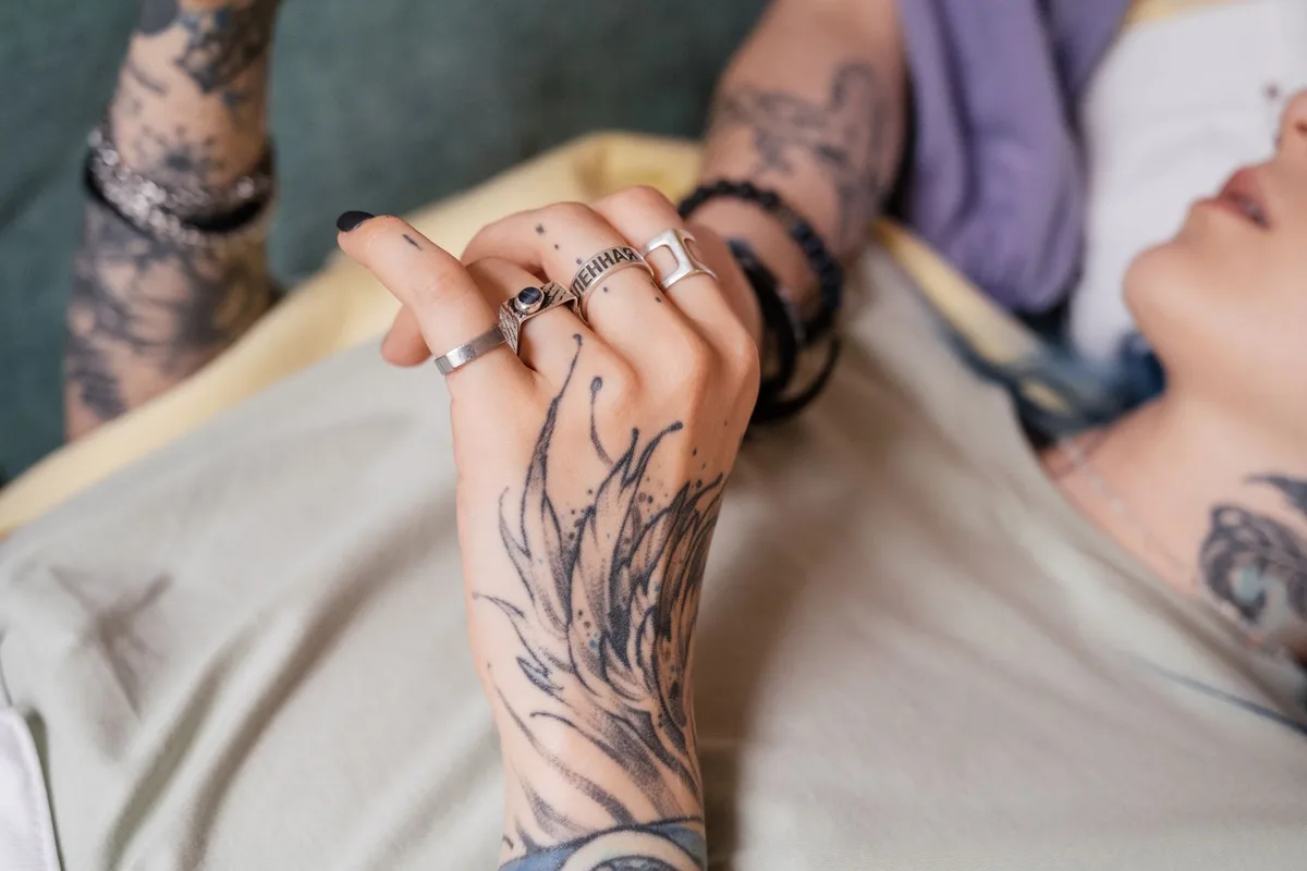A close-up of a tattooed hand with silver rings, showcasing intricate designs and fashion.