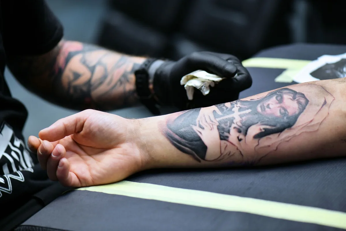 A tattoo artist creating detailed artwork on a person's arm in an indoor studio setting.