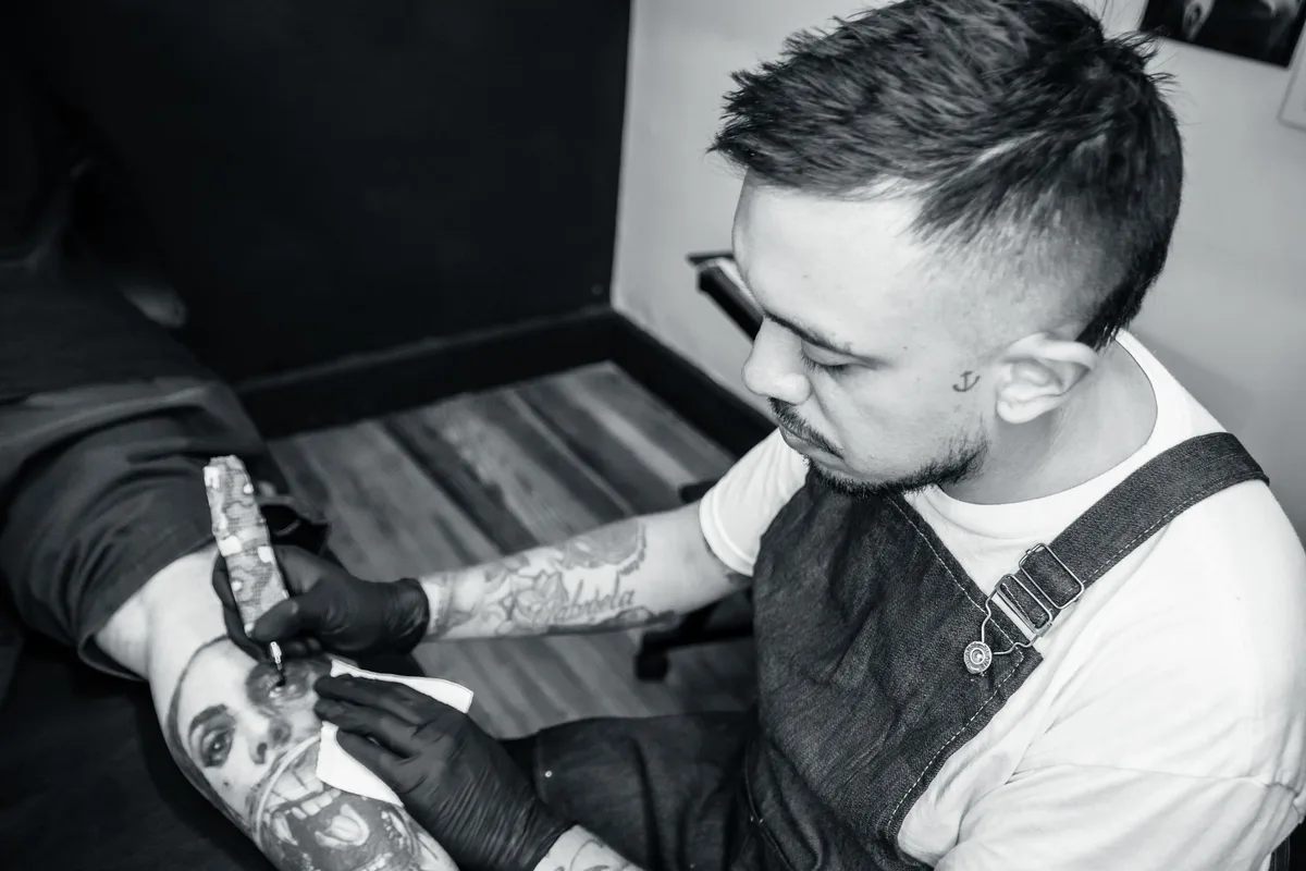 Tattoo artist focused on creating a detailed tattoo on a client's leg in a studio setting.