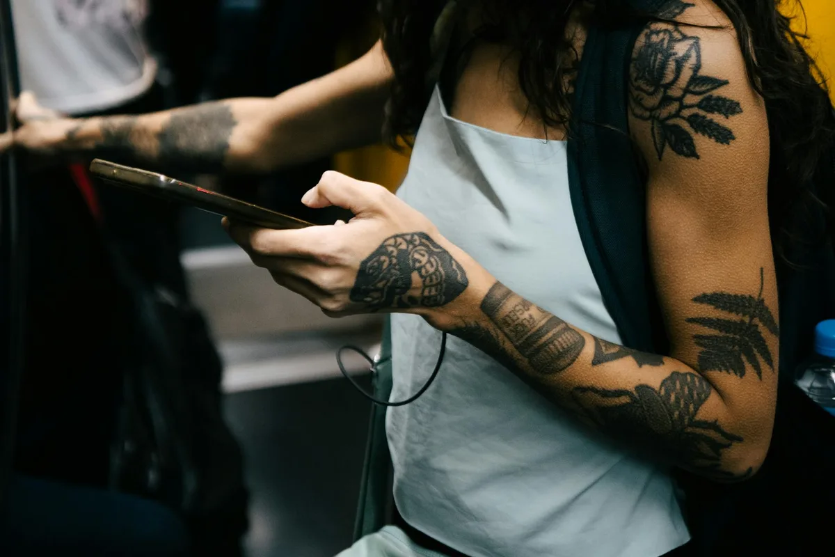 A person with tattoos using a smartphone on public transportation, showcasing modern lifestyle.